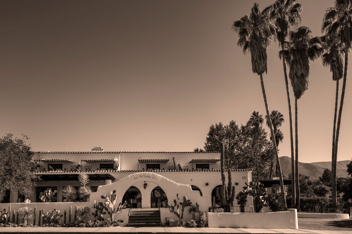 Black and white facade of Hotel El Roblar with tall palm trees